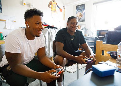 housing - two male students play video games in dorm room